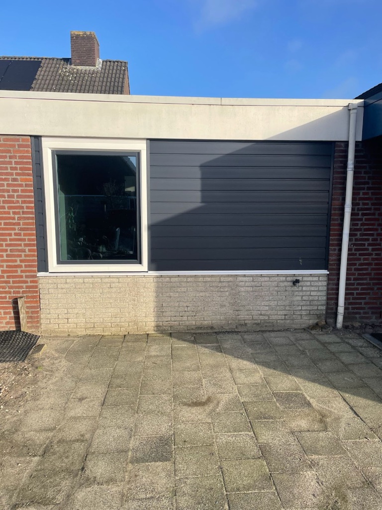Donkere gevelbekleding naast een kozijn